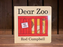 Load image into Gallery viewer, Image of the cover of the board book Dear Zoo. It has a cream background, with an illustration of a lion, with the head hidden, in a red box with a note saying &#39;from the zoo&#39;. The title is in plain black text. 