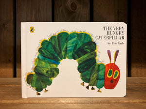 Image of the front cover of The Very Hungry Caterpillar. It has a white background, and an illustration of a green caterpillar with a red face. The title is written in plain black text.
