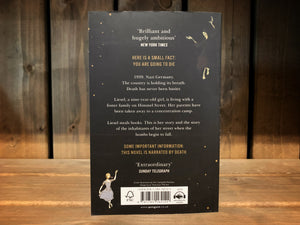 Image of the back cover of The Book Thief. The cover is black, with a few yellow dots/stars in the upper left and bottom right corner. On the opposite corners are the illustrations of death and the girl dancing. The blurb is written in the middle in yellow and white text.