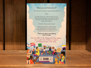 Image shows the back cover of Jamie. The illustration of the crowd continues, carrying more flags and signs with positive LGBT+ messages. the blurb is written in black text.