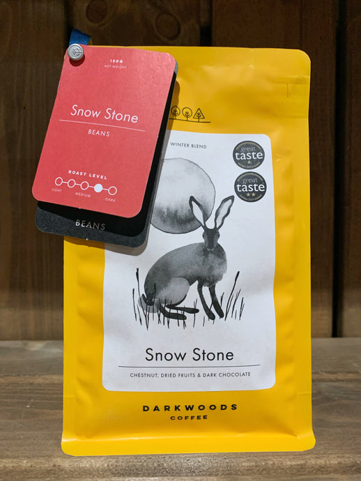 Image of the Roasted Magic Beans (Whole) - Snow Stone coffee beans. The image shows a bright yellow packet with a black and white drawing of a rabbit/hare in front of the moon. There are two labels attached to the top left corner of the packet with the name of the coffee, the fact that it is decaf, and the label underneath states that they are beans.