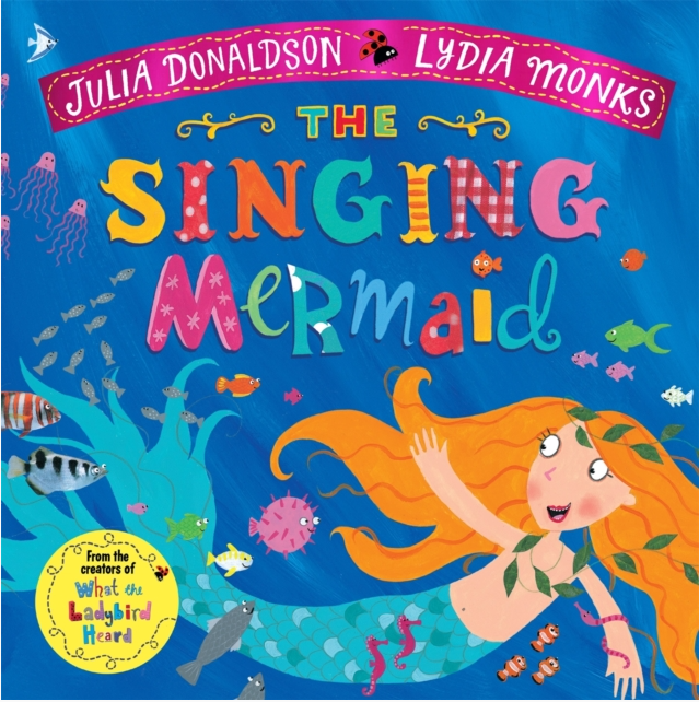 Image shows the front cover of paperback book The Singing Mermaid by Julia Donaldson and illustrated by Lydia Monks. Illustration shows a mermaid with orange hair and blue tail in the sea with shoals of fish. Title text is illustrated in various patchwork styles and colours. 