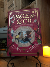 Load image into Gallery viewer, Image of the front of the hardback book Pages and Co: Tilly and the Map of Stories written by Anna James and illustrated by Paola Escobar. Displayed on a book stand with candles.