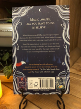 Load image into Gallery viewer, Image of the back cover of the paperback book The Castle of Tangled Magic, written by Sophie Anderson and illustrated by Saara Soderlund. Displayed on a book stand with candles.