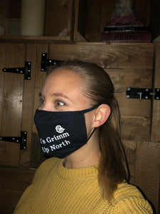 Image shows black jersey face mask printed with white text slogan saying 'It's Grimm Up North' with the Grimm & Co 'G' monogram, mask is shown displayed on an adult head.