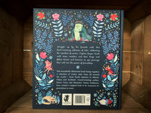 Load image into Gallery viewer, Image of the back of the book Winter Tales. The back cover is dark blue, with the blurb in the center written in pale blue text. The  illustrations of flowers and stars continue from the front, and there are also illustrations of an old man with a staff, fairies, witches, and a fox and a mouse. 