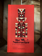 Load image into Gallery viewer, Image showing the front cover of The Nutcracker. The cover is clothbound and red, featuring an illustration of the traditional nutcracker soldier by Sanna Annukka.