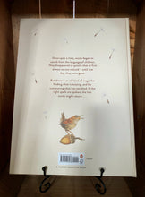 Load image into Gallery viewer, Image of the back of the book The Lost Words. The cover has a white/cream background, with illustrations of falling dandelion seeds, and at the bottom a small illustration of a wren standing on an acorn. The blurb is written in the center in brown text.