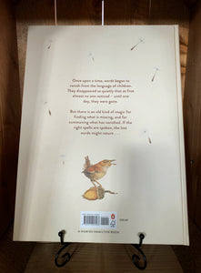 Image of the back of the book The Lost Words. The cover has a white/cream background, with illustrations of falling dandelion seeds, and at the bottom a small illustration of a wren standing on an acorn. The blurb is written in the center in brown text.