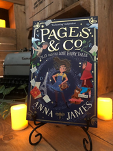 Load image into Gallery viewer, Image of the front of the paperback book Pages &amp; Co: Tilly and the Lost Fairy Tales written by Anna James, and illustrated by Paola Escobar. Displayed on a book stand with candles.
