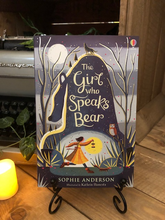 Load image into Gallery viewer, Image of the front cover of the paperback book The Girl Who Speaks Bear, written by Sophie Anderson and illustrated by Kathrin Honesta. Displayed on a book stand with candles.
