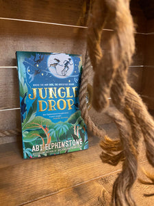 Image shows the front cover of the paperback book Jungle Drop by Abi Elphinstone on a wooden shelf with rope