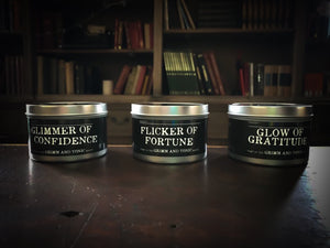 Image showing all three tinned candles in the Grimm & Tonic range including Glimmer of Confidence, Flicker of Fortune and Glow of Gratitude. Candles in silver tins with black labels and white text
