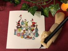 Load image into Gallery viewer, Image of a festive greetings card showing a cartoon illustration of three shop elves amid present wrapping and snacks drawn by Chris Mould. Display shows a wooden mannequin hand holding a Dip Wand poised to write a card