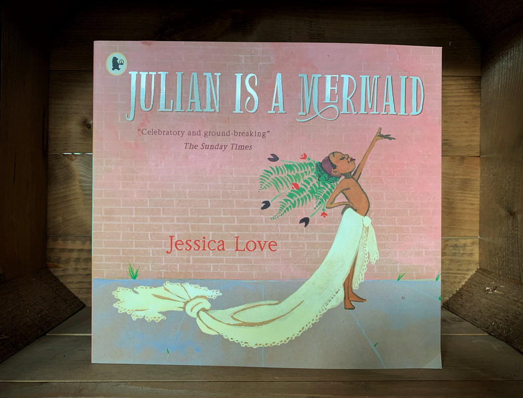 Image of the front of the book Julian is a Mermaid. The cover shows a black boy wearing a sheet around his waist, trailed and tied up to look like a tail, and a flower headdress, standing on a street side. 