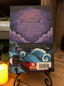 Image of the back of the paperback book Moonchild Voyage of the Lost and Found by Aisha Bushby and illustrated by Rachael Dean. Displayed on a book stand with candles.