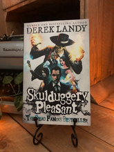 Load image into Gallery viewer, Image of the front of the paperback book Skulduggery Pleasant by Derek Landy. Displayed on a book stand.