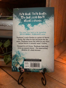 Image of the back of the paperback book Skulduggery Pleasant by Derek Landy. Displayed on a book stand.