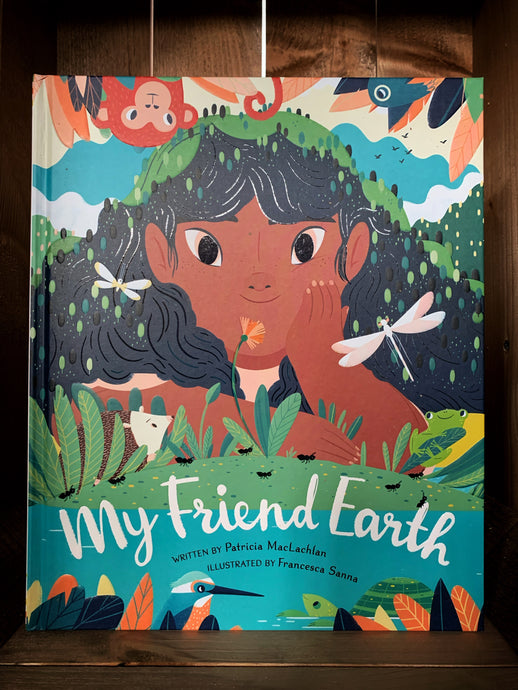 Image of the front cover of the book My Friend Earth.  The cover shows an illustration of a close up of a girls face as she leans on the ground by a river. She is surrounded by plantlife, and a variety of birds, animals, and insects. 