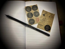 Load image into Gallery viewer, Image shows the inside of the red notebook with lined white paper and detail of the set of 12 stickers printed with slogans such as &#39;Fee Fi Fo Fum, Once upon a time&#39; and images including a magica wand, hook hand and potion bottles. Image also shows close up of Word Wand pencil which has Grimm &amp; Co writeen on one side, and at the top end and arrow stating magic, and the bottom end and arrow and saying mistakes pointing to the eraser.