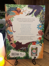 Load image into Gallery viewer, Image of the back cover of the hardback book of Aesop&#39;s Fables stood in a book stand with candles