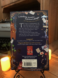 Image of the back of the paperback book Pages & Co: Tilly and the Lost Fairy Tales written by Anna James and illustrated by Paola Escobar. Displayed on a book stand with candles.