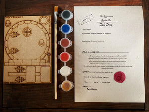 Image shows the contents in a fairy door pack. A door and accessories (version in photograph is a round edition), a paintbrush, a set of five paints, and a title deed activity sheet.
