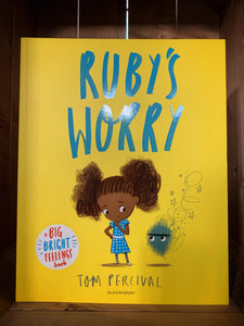Image of the front cover of the book Ruby's Worry. The cover has a bright yellow background, and an illustration of a black girl looking worriedly at a small, grey, angry scribbled creature hovering next to her.