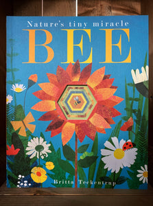 Image shows the front cover of the paperback book, Bee: Nature's Tiny Miracle. The cover features paper cutout -style illustrations of flowers in green, white, yellow, and orange on a bright blue background.  A large orange flower in the center has the first cut out (that continues throughout the entire book),  showing a picture of a small bee that is on the final page. 