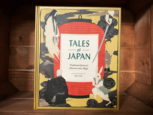 Image of the front cover of the book Tales of Japan. The cover has a matte gold background, with an illustration of a  large red paper lantern in the center, where the title is written in black text in a white square.  Surrounding it are traditional Japanese style illustrations of characters and objects featured within the stories inside, including a rabbit in a sleeveless jacket, a hand holding a sword, and a floating ghostly lady with long black hair. 