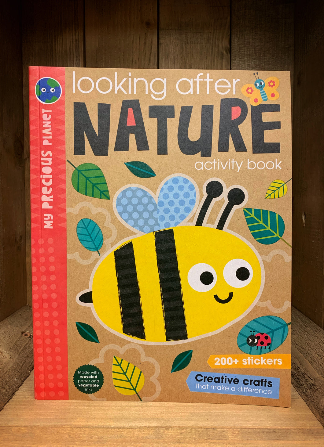 Image of the front cover of Looking After Nature Activity Book. Cover has a Kraft brown background with a red spine, and a cartoon style illustration of a bee surrounded by green leaves.