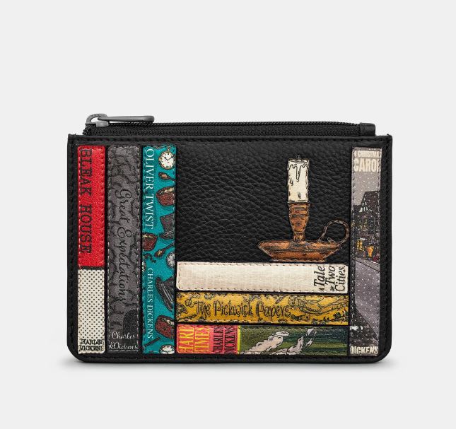 Image shows the black Yoshi leather sip top coin purse featuring appliqued book spines with titles written by Charles Dickens and a candle in a candle holder sat on top of a stack of books. Titles include A Tale of Two Cities, A Christmas Carol, Oliver Twist and Hard Times.