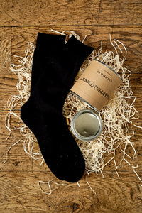 Image of an example black sock next a tin of disappointment laying on its side in a nest of wood wool with the lid removed.