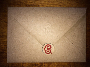Detail of the kraft brown envelope with the embossed Grimm & Co 'G' monogram on the flap, and a sticker used as an envelope seal