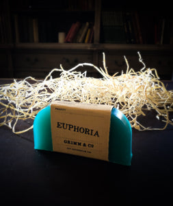 Image of a Euphoria bar, a teal green solid shampoo slice with a kraft paper label