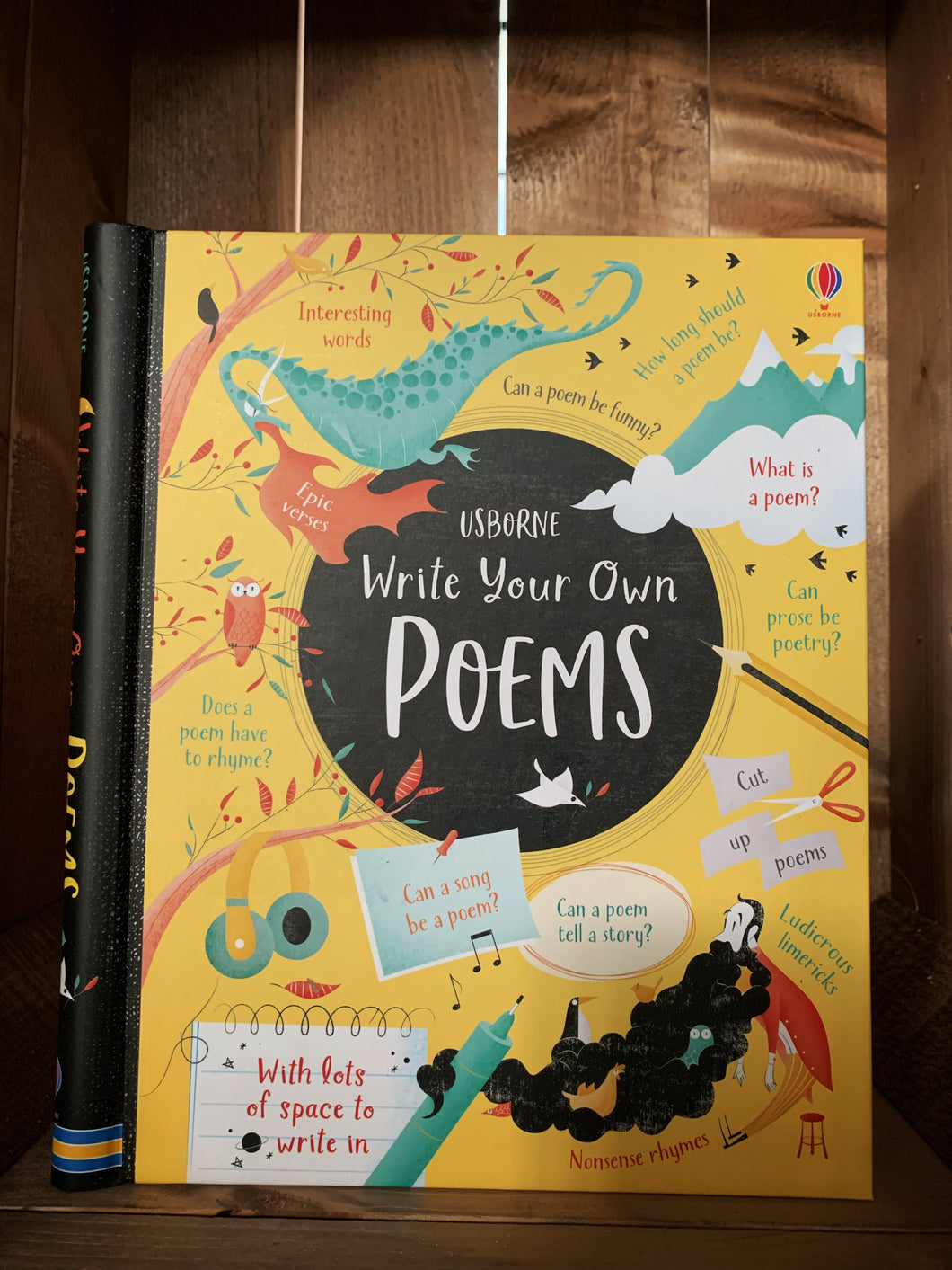 Image of the front of the book Write Your Own Poems. The cover background is bright yellow with a red spine. The title is written inside a black circle in the center. Surrounding the circle are various illustrations, including a dragon, mountains, pens and pencils, and  man with a long black beard full of types of birds. There are small amounts of text around the images explaining what the book can help with, including what is a poem, and does a poem have to rhyme. 