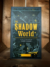 Load image into Gallery viewer, Image of the front of the box for The Shadow World: Storytelling Card Game. The background is dark grey, with an illustration of a factory in black and light grey, with cogs, wheels, pipes, and stairs leading up to a lit up town on a platform at the top of the box, with various animals, robots, fish and individuals scattered throughout. The title is in the center in bright yellow text. 