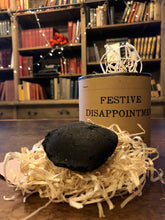 Load image into Gallery viewer, Image shows a tin of Festive Disappointment with kraft paper label, lid is open showing wood wool shreds and a lump of black coal 