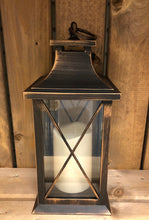 Load image into Gallery viewer, Image showing a bronze coloured Bright Ideas lantern with a large X lattice pattern on the windows with a battery operated candle inside and a handle on the top.