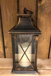 Image showing a bronze coloured Bright Ideas lantern with a large X lattice pattern on the windows with a battery operated candle inside and a handle on the top.