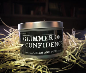 Image of the Glimmer of Confidence, a tinned candle with slip lid in the Grimm & Tonic range with a black label and white text.