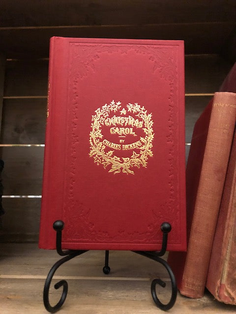 Image shows the front cover of the hardback book A Christmas Carol with a red clothbound cover and gold foil lettering. 