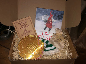 Image of the Gift Box to Mull Over containing the hardback book Letters From Father Christmas, spiced apple juice sachet, a giant chocolate coin, a knitted elf hat decoration and a jute drawstring pouch of edible elf staffs, all presented in a kraft cardboard box filled with wood wool.