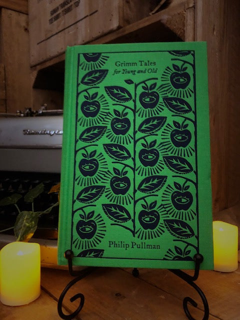 Image of the clothbound hardback book Grimm Tales For Old and Young by Philip Pullman. The cover is bright green, with navy branches holding leaves and apples with eyes in the center.