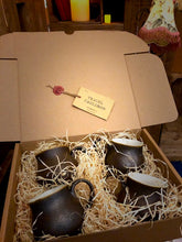 Load image into Gallery viewer, Image of a set of four Travel Cauldrons,  otherwise known as matte black ceramic mugs, nestled in wood wool in a cardboard box. A Travel Cauldron label is wax sealed to the inner lid of the box.