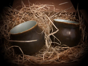 Image of two Mini Travel Cauldron espresso cups without handles nestled in a box with wood wool packaging.