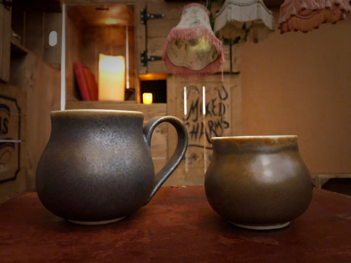 Image of both sizes of Travel Cauldron, regular and mini. Travel Cauldrons are more commonly known as mugs in the mortal realm, ceramic and dyed a rich copper to black colour, each one is unique and handmade. The regular sized mug has the Grimm & Co 'G' monogram stamped into the base of the handle.