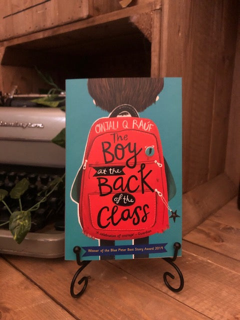 Image of the front cover of the paperback book The Boy at the Back of the Class written by Onjali Q Raúf and illustrated by Pippa Curnick. Displayed on a book stand.