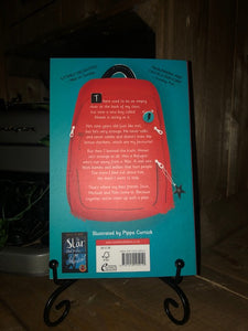 Image of the back cover of the paperback book The Boy at the Back of the Class written by Onjali Q Raúf and illustrated by Pippa Curnick. Displayed on a book stand.