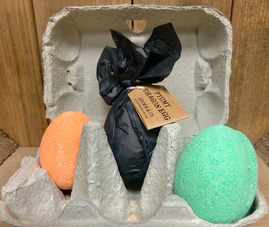 Image of three Pygmy Dragon Eggs sat inside an egg carton, one is wrapped and labelled how it will arrive if ordered, the other two are unwrapped to show the shape and various colours.